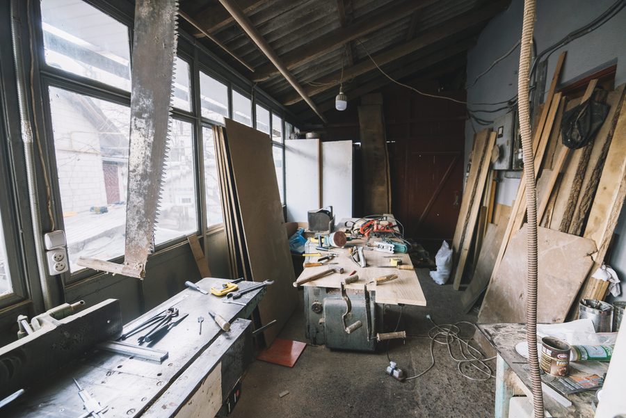 A cluttered garage workshop filled with timber, hand tools and a crowded workbench